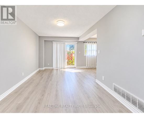 A spacious room with light wood flooring and white walls, with a sliding glass door leading to a garden.