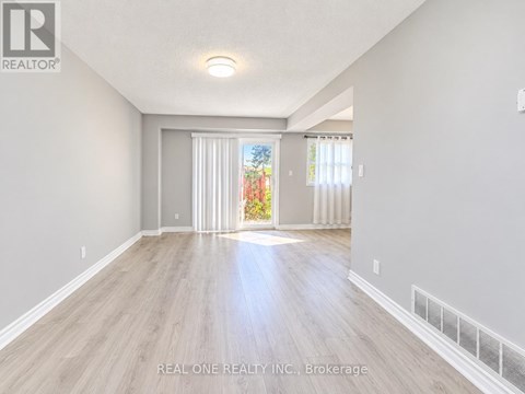 A spacious room with light wood flooring and white walls, with a sliding glass door leading to a garden.