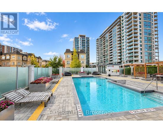 A pool surrounded by a glass fence with a bench and flower bed.