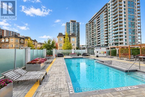 A pool surrounded by a glass fence with a bench and flower bed.