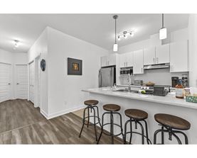 A kitchen with white cabinets and a bar area with stools.