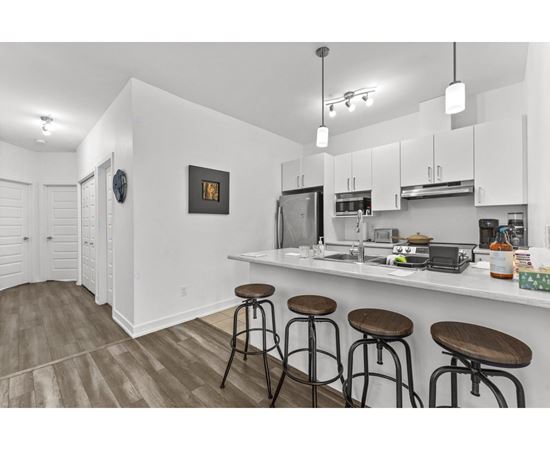 A kitchen with white cabinets and a bar area with stools.