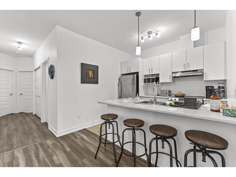 A kitchen with white cabinets and a bar area with stools.