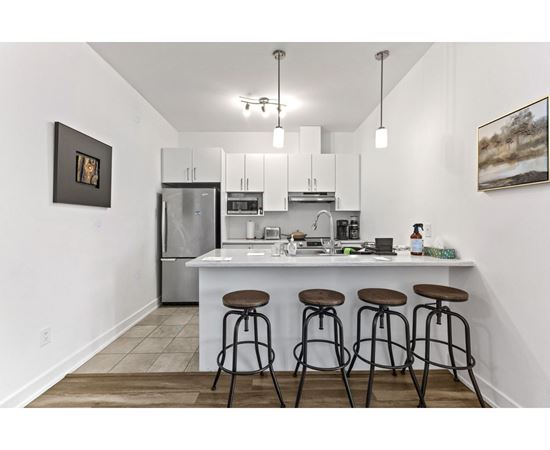 A kitchen with white cabinets and a white island with three stools.