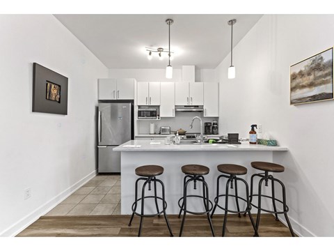 A kitchen with white cabinets and a white island with three stools.