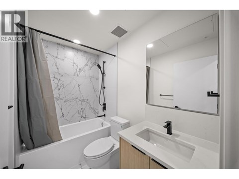 A white bathroom with a marble patterned shower wall.