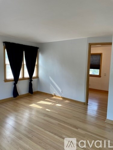 A room with wooden flooring and a window with black curtains.