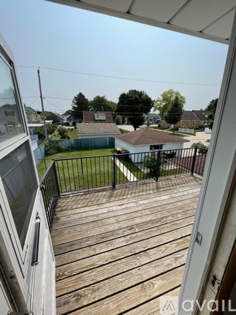 A balcony with a black railing and a wooden floor overlooks a residential area.