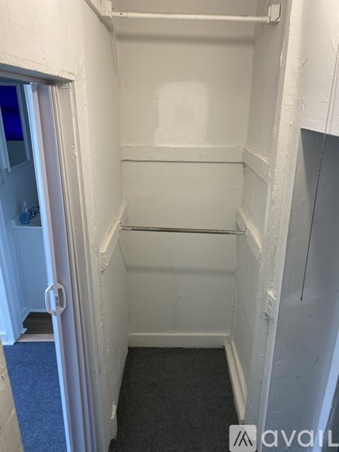 A small, white, empty room with a door on the left.