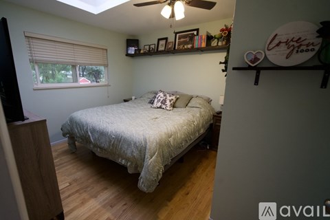 A bedroom with a bed, a window with blinds, a ceiling fan, and a shelf with decorative items.