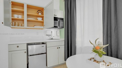 A kitchen with a refrigerator, microwave, and a cabinet with glass doors.