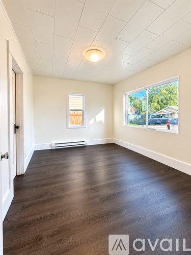 A room with wooden floors and a window showing a view of a house and trees.