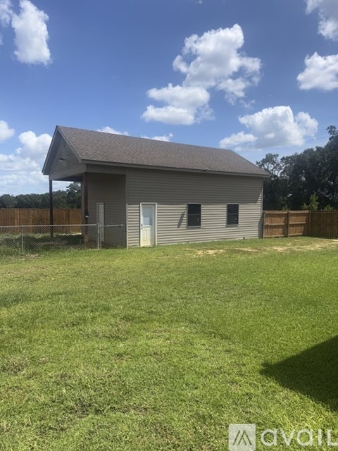 A small building with a grey roof is surrounded by a grassy field.