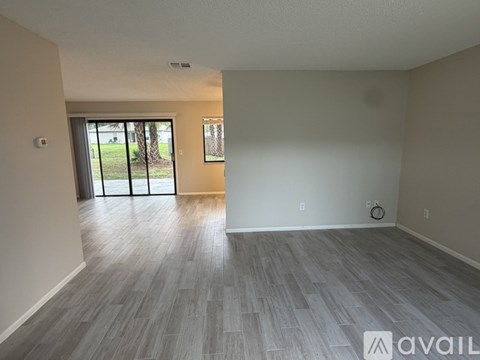 A spacious room with a grey floor and a sliding glass door leading to a green outdoor area.