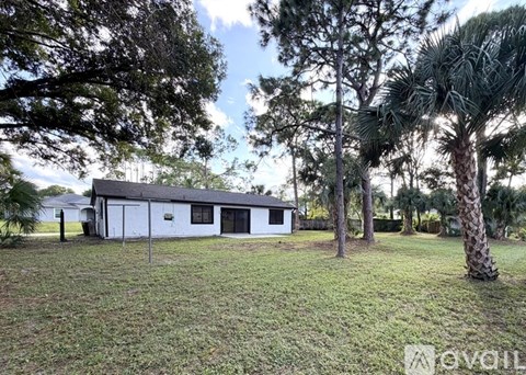 A small white house is surrounded by trees and grass.