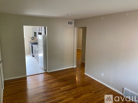A room with wooden floors and a white wall with a doorway leading to another room.