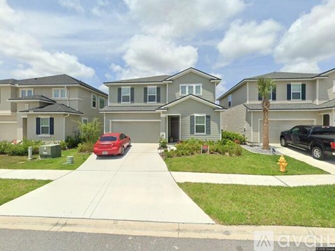 A red car is parked in front of a grey house.