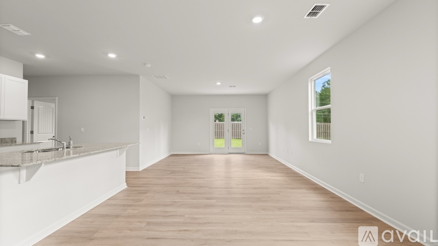 A spacious room with wooden flooring and white walls, featuring a kitchen area with a sink and a window.