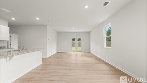 A spacious room with wooden flooring and white walls, featuring a kitchen area with a sink and a window.