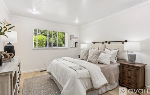 A bedroom with a large bed, a nightstand, and a window with blinds.