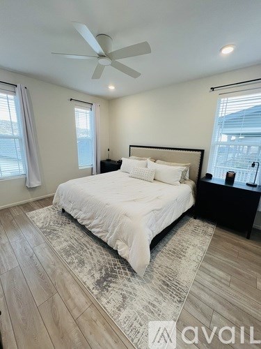 A bedroom with a large bed, a ceiling fan, and a window with white curtains.