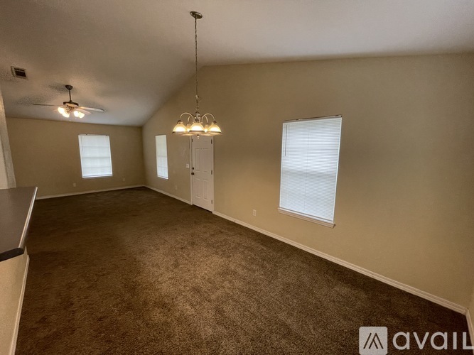 A spacious room with carpeted floor, ceiling fan, and a chandelier.