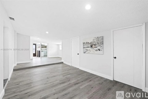 A spacious room with wooden flooring and white walls.