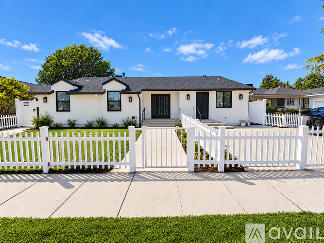 A white house with a black door and windows is surrounded by a white picket fence.