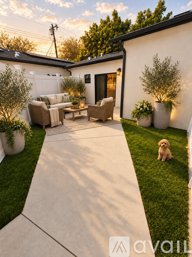 A dog sits on the grass in front of a house with a patio.