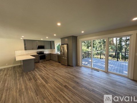 A spacious room with wooden flooring and a large window overlooking a patio.