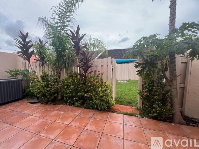 A patio with a tiled floor surrounded by green plants and trees.