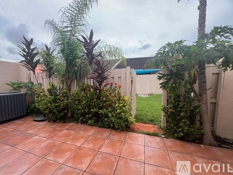 A patio with a tiled floor surrounded by green plants and trees.