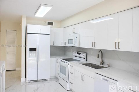 A white kitchen with a refrigerator, microwave, oven, and sink.