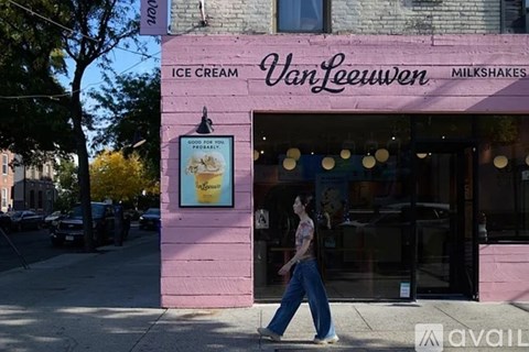 A woman walks past a pink building with a sign that says "Van Leeuwen Ice Cream Milkshakes.".