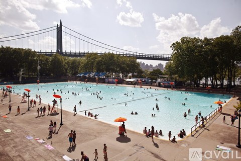 A large outdoor swimming pool with people in it and a bridge in the background.