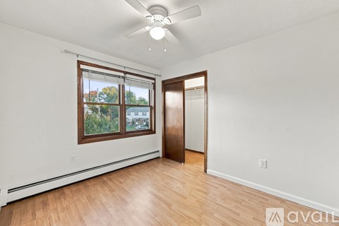 A room with a ceiling fan and a window with a view of trees and a building outside.