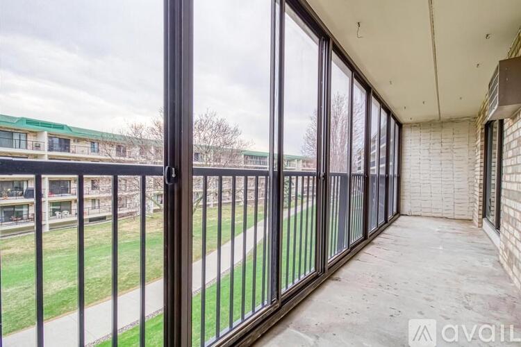 A balcony with a metal railing and a view of a grassy area and buildings.