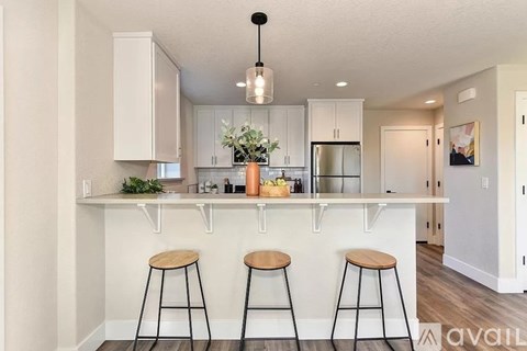 A kitchen with white cabinets and a bar area with three stools.