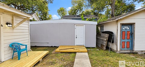 A small white building with a blue door is surrounded by a wooden deck and a small garden.