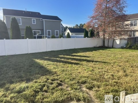 A white fence separates a grassy area from a residential area.