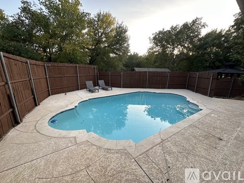 A small kidney-shaped pool surrounded by a concrete patio and a wooden fence.