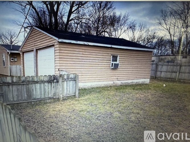 A house with a brown siding and a white garage door is surrounded by a wooden fence.