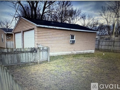 A house with a brown siding and a white garage door is surrounded by a wooden fence.
