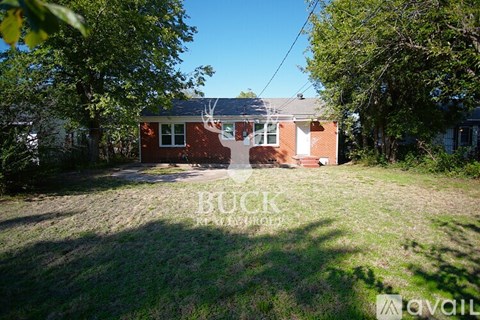 A red brick house with a white door and windows is surrounded by trees and grass.