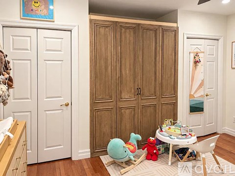 A room with a white door, a wooden wardrobe, a table with toys and a chair.