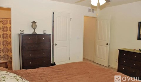 A bedroom with a brown bedspread and a brown dresser with a lamp on top.