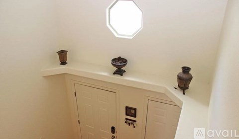 A white hexagonal window in a white room with a cabinet underneath it.