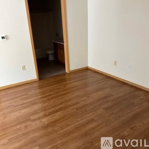 A room with wooden flooring and a doorway leading to another room.