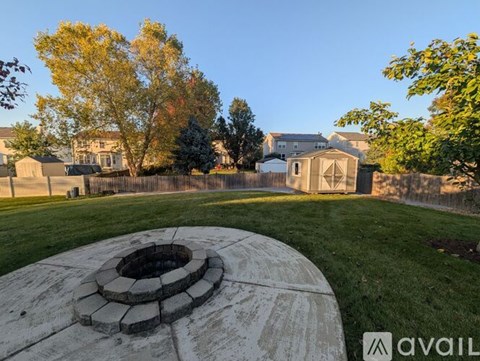 A stone fire pit sits in the middle of a grassy area with a residential neighborhood in the background.