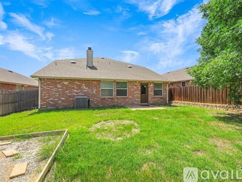 A house with a brown roof and a brick exterior is surrounded by a wooden fence and has a green lawn.